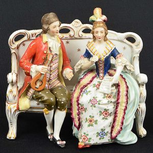 <b>Grupo escultórico</b> em porcelana europeia policromada representando casal de nobres sentados, com elaborados trajes. Marca da manufatura no verso. Séc. XVIII / XIX. Med. 17,5 x 17,5 x 10 cm