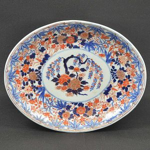 <b>Travessa</b> oval em porcelana "Imari" apresentando rica decoração com flores em suas tonalidades características de azul índigo, "rouge de fer" e ouro sobre fundo branco. Séc. XIX. Med. 37,5 x 30 cm