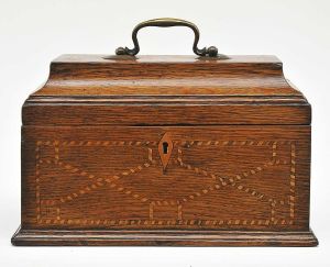 Antiga <b>caixa</b> inglesa, em forma de pequeno baú, em carvalho, decorada com filetes de "marcheterie" e alças metálicas. Med. 16 x 25,5 x 14 cm