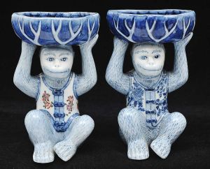<b>Par de estatuetas</b> chinesas em porcelana policromada em forma de macaquinhos sustentando cestas. Alt. 21,5 cm