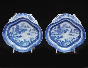 <b>Par de covilhetes </b>em forma de "coquilles", em porcelana Vista Alegre decorada em azul índigo com paisagem com duas personagens e edificações orientais. Med. 21 x 20,5 cm