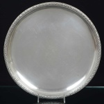 <b>Bandeja </b>circular em prata apresentando fundo liso e borda em trevos. Contraste e marca do prateiro. Diâm. 34,5 cm. Peso 1.540 gramas